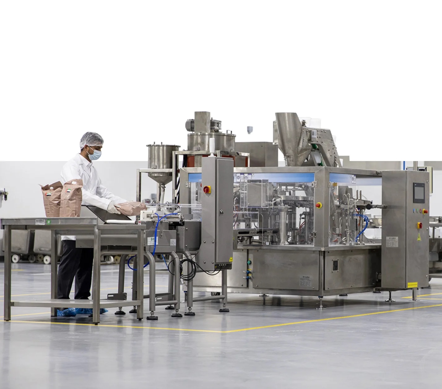 An ARZAAQ technician in full hygiene dress turning the handwheel of a steam-jacketed cooking kettle on the production floor.